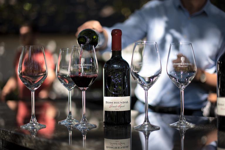 Wine glasses and red wine bottle, hand pouring wine into a glass.