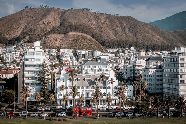 White hotel building with palm trees in front, more white buildings in the background, palm trees, and Table Mountain in the background.