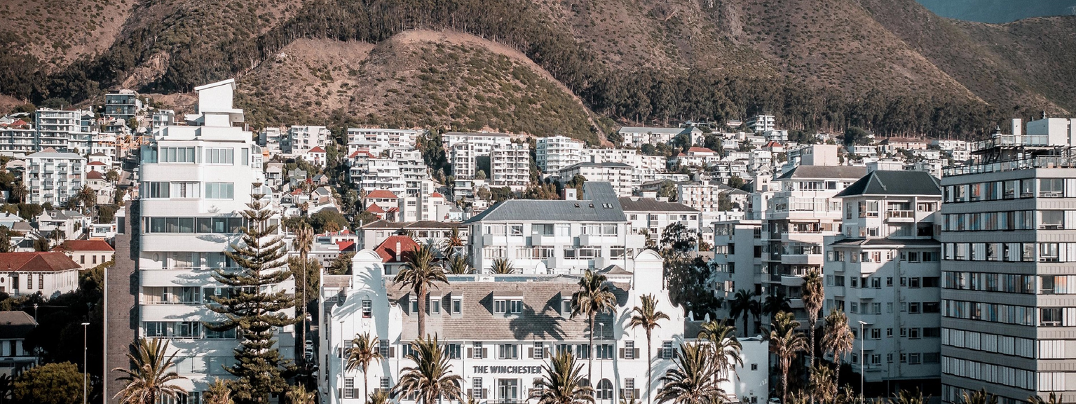 White hotel building at the forefront, surrounded by white buildings, palm trees in near distance.